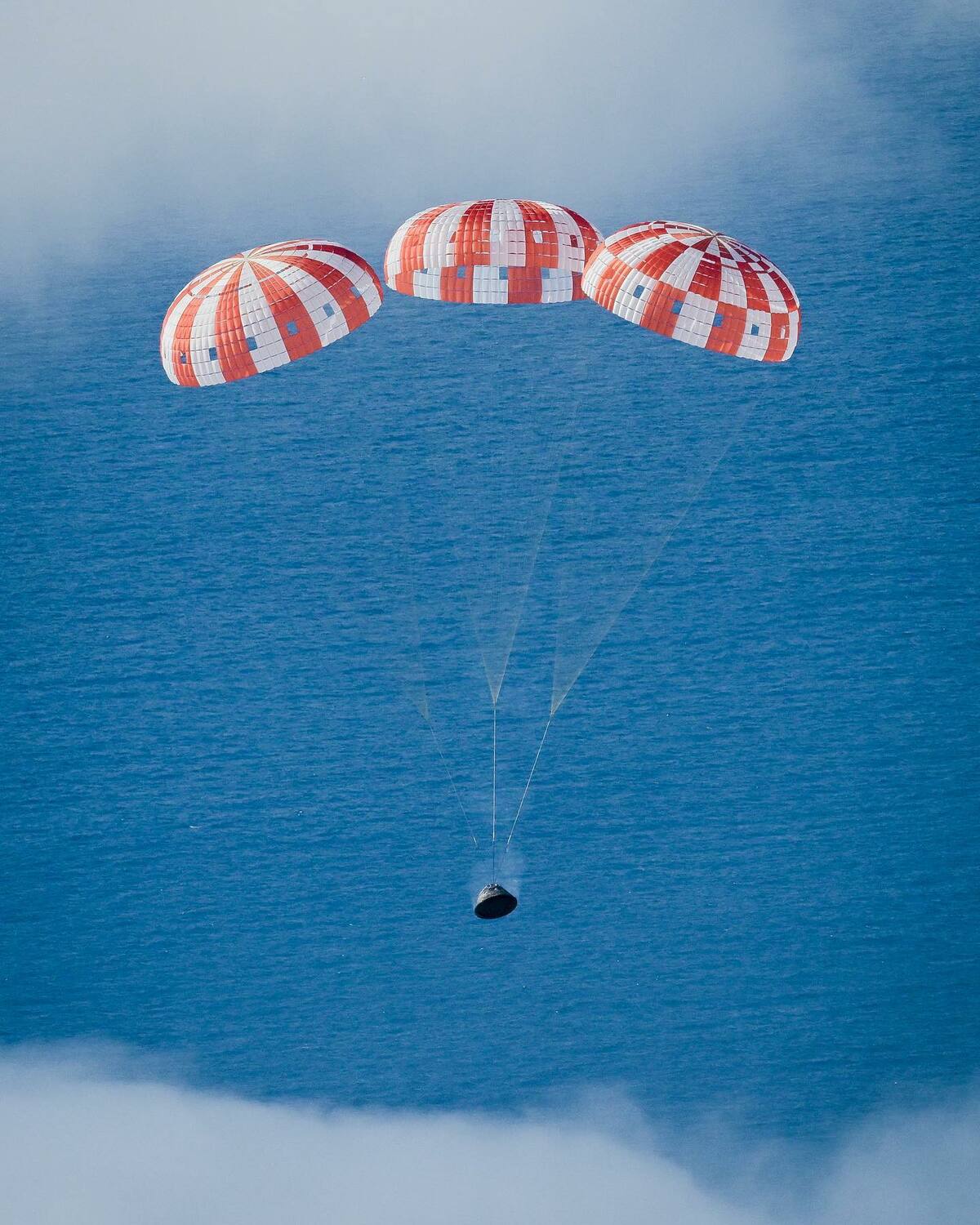 美國航空暨太空總署「阿提米絲1號」(Artemis Ⅰ)所搭載的「獵戶座」(Orion)太空船在3頂降落傘的輔助下重返地球「濺落」海面。 圖：翻攝@NASA_Orion推特