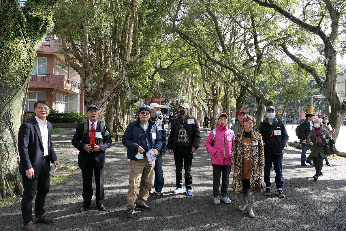醒吾科大副校長鍾志明（左）帶領畢業50年校友漫步林蔭大道，回想當年的小樹如今已茁壯成大樹，校友們滿臉甜蜜笑容。 圖：醒吾科大提供
