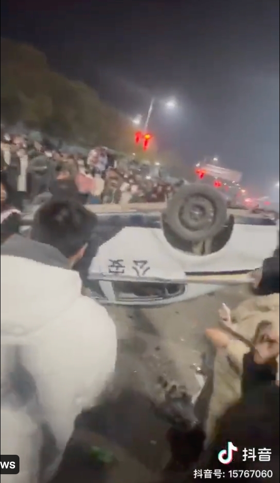 幾名年輕人不滿警察魯莽執法，憤而躍上警車示威，在大批民眾包圍下，車牌遭拆落，車輛並被直接掀起，更有人索性將鞭炮朝向警車方向施放。 圖：截自推特@whyyoutouzhele