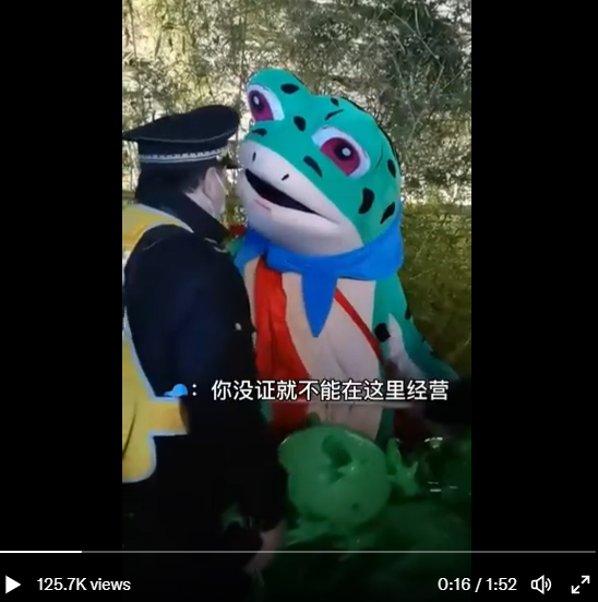 中國一名身穿青蛙裝的人違法在路邊販賣氣球，遭城管取締。 圖：翻攝自推特@dbezuqun
