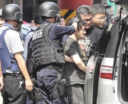 新北市中和興南觀光夜市30日發生警匪駁火案件，嫌犯 劉邦誠（前右）躲進1處公寓與警方對峙逾3個小時，下午三點多終於棄械投降，由警方帶回新店分局偵訊。 圖:中央社