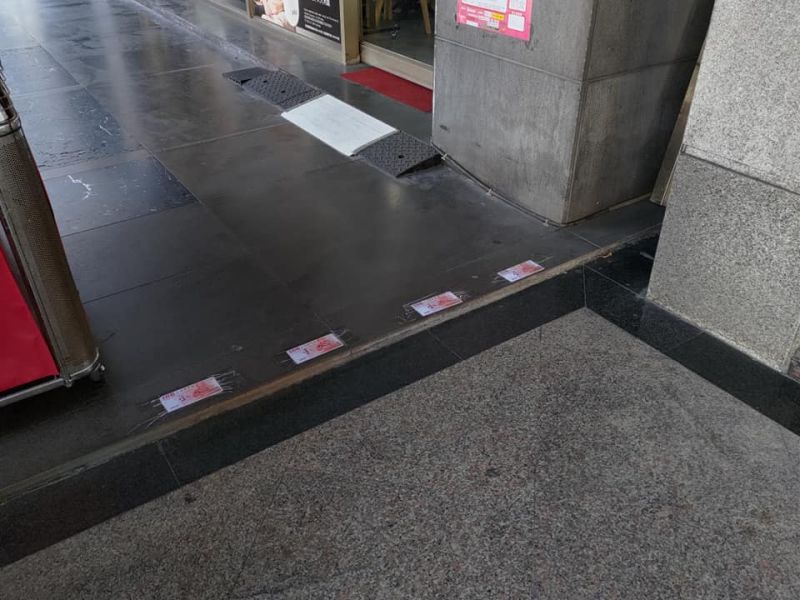 ▲有民眾在一間銀行外騎樓時，突然看到地面上被貼著4張百元鈔票，讓他忍不住彎下腰靠近仔細看。（圖／《路上觀察學院》）