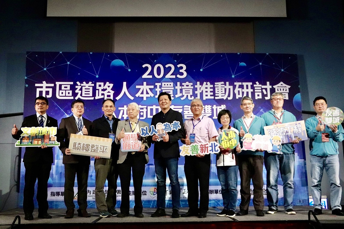 新北市副市長朱惕（中）、工務局長祝惠美（右4）、養工處長簡必琦（右3）與產官學界學者拿著以友善通行環境為主的舉手牌們，一同合影留念。 圖：新北市工務局提供