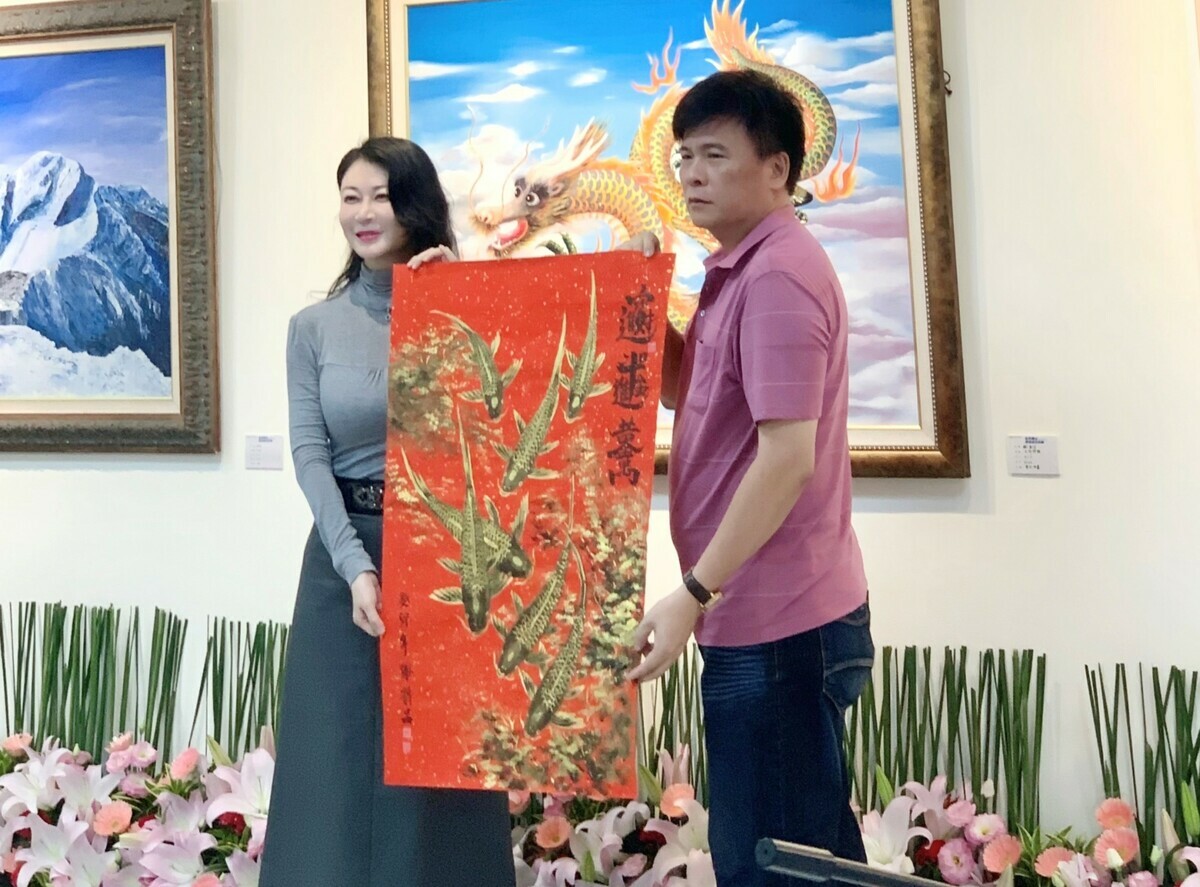 策展人謝新昌(右)將「金玉滿堂」畫作贈予劉嘉茹。 圖：高雄市立空中大學提供