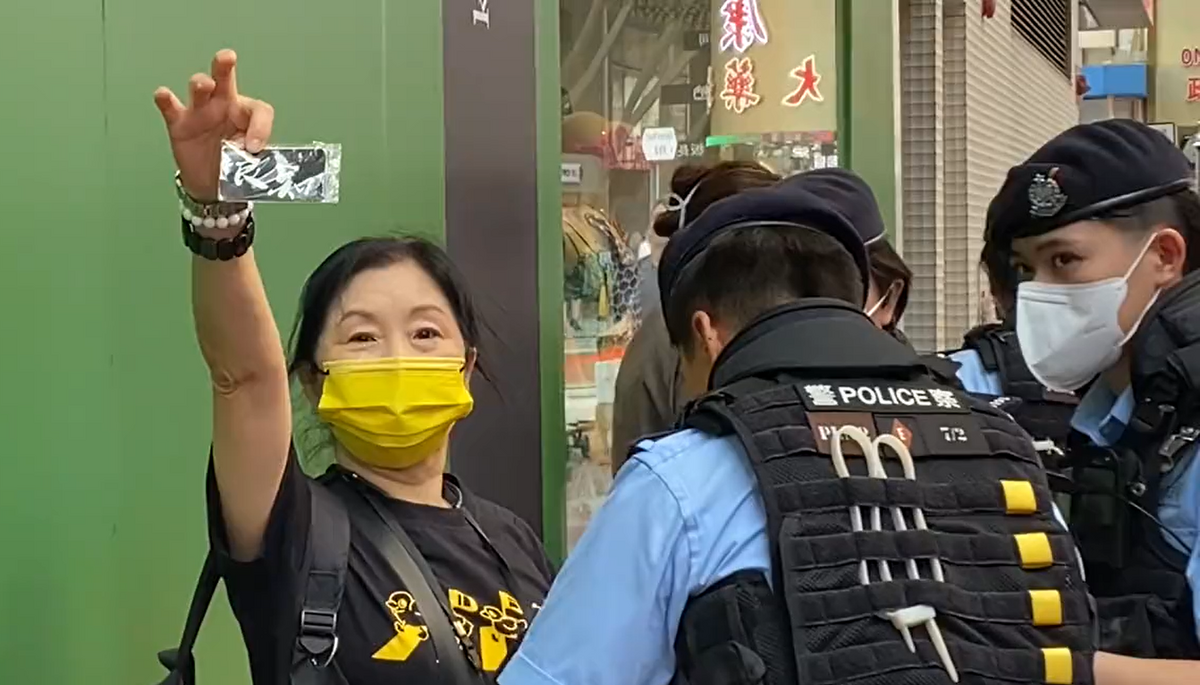 有一位香港女士，被多名警察搜查時，看到圍觀拍攝者，淡定從包包裡拿出寫著「良知」的卡片。 圖：翻攝自彥子lanni推特