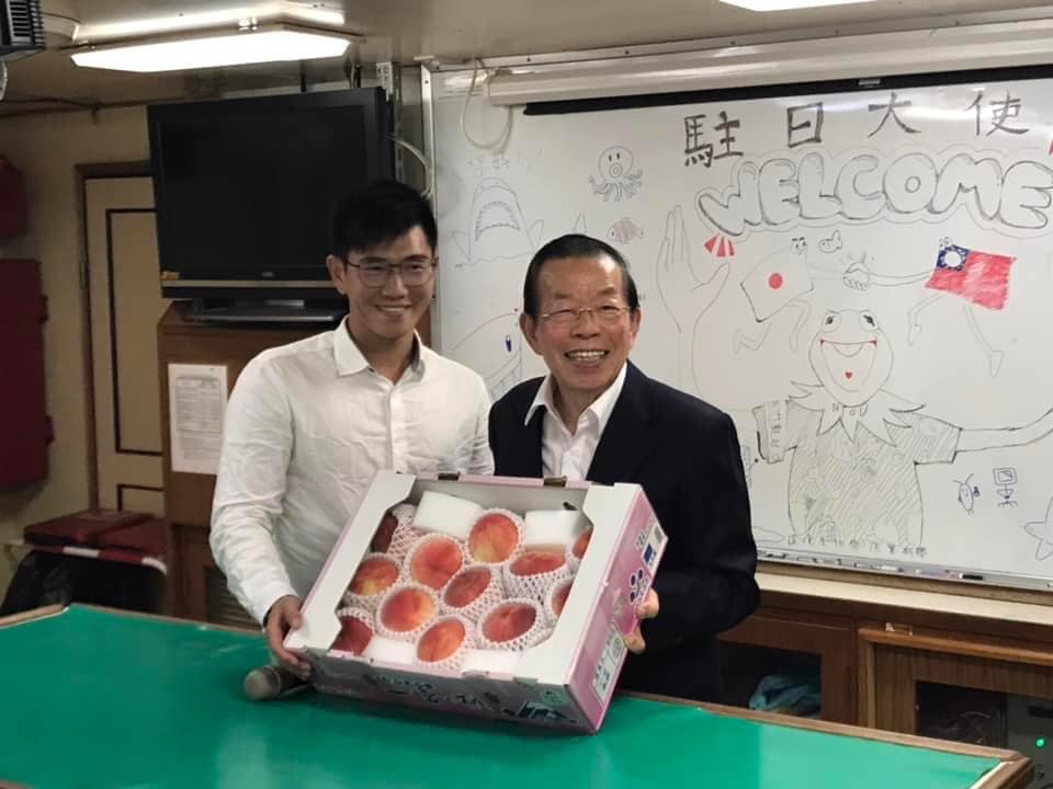 漁業署「漁訓貳號」漁業訓練船停靠日本東京晴海碼頭，我駐日代表謝長廷（右）特地致贈日本的桃子，背後白板上的歡迎詞寫著大大的「駐日大使」4個字。 圖：翻攝自謝長廷臉書