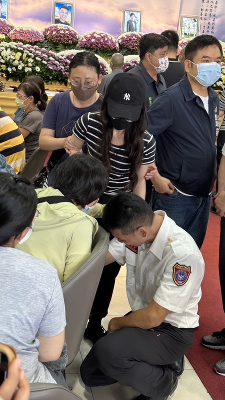 屏東縣消防局屏二分隊分隊長李炯佑（前右白衣者）24日前往屏東明揚工廠爆炸意外殉職消防人員靈堂，一度情緒崩潰，單膝跪地哭倒在殉職隊員施寶翔家屬身旁，現場氣氛悲淒。 圖：中央社（民眾提供）