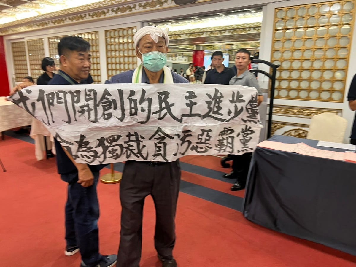 民進黨創黨人之一的魏耀乾今（27）日在民進黨創黨餐會的會場外，高舉「我們開創的民進黨，已淪為獨裁貪污惡霸黨」布條抗議。 圖：林朝億攝  （資料照）