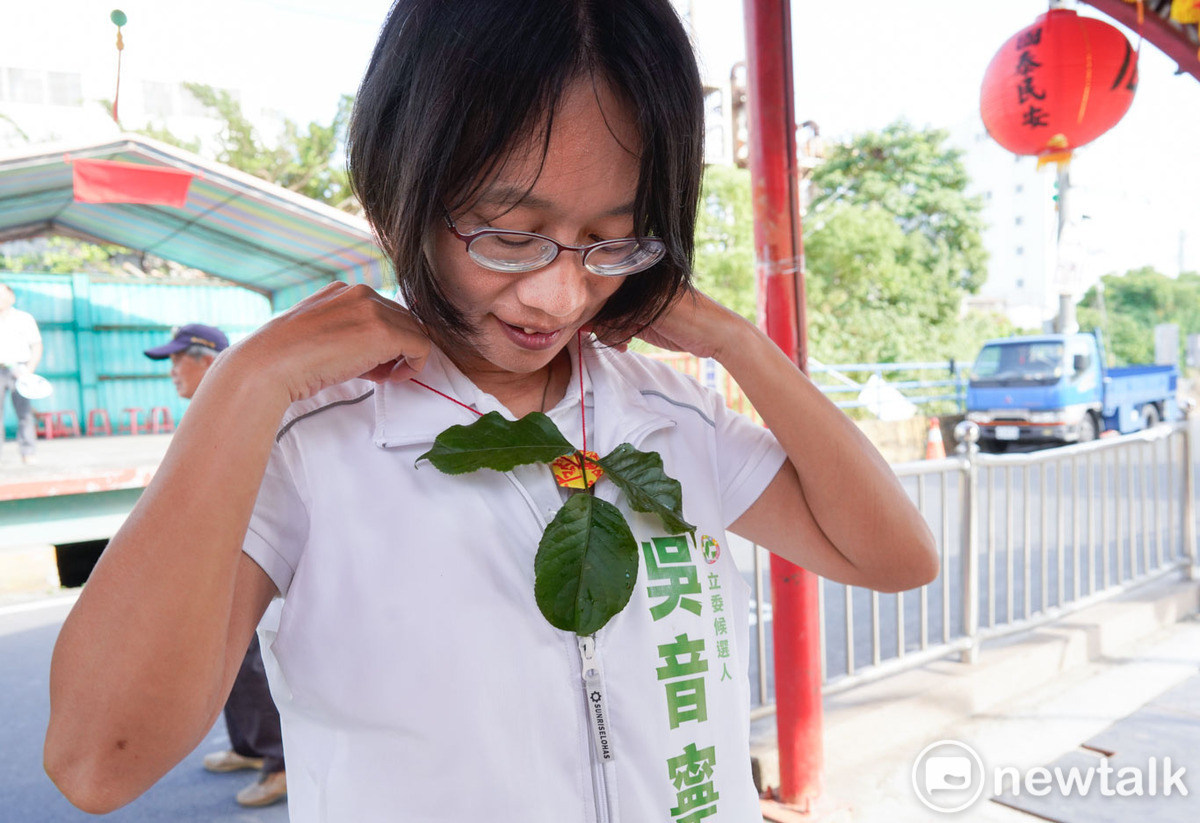 吳音寧到埔心鄉太平村茄苳公向拜拜的村民拜票時，將茄苳樹公的茄苳葉、銅錢和平安符製作成貫絭掛載脖子上，祈求茄苳樹公的庇佑。 圖：張良一/攝