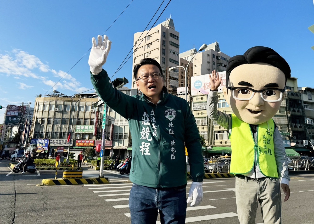 莊競程與Q版大頭娃娃站路口拜票。 莊競程競總/提供