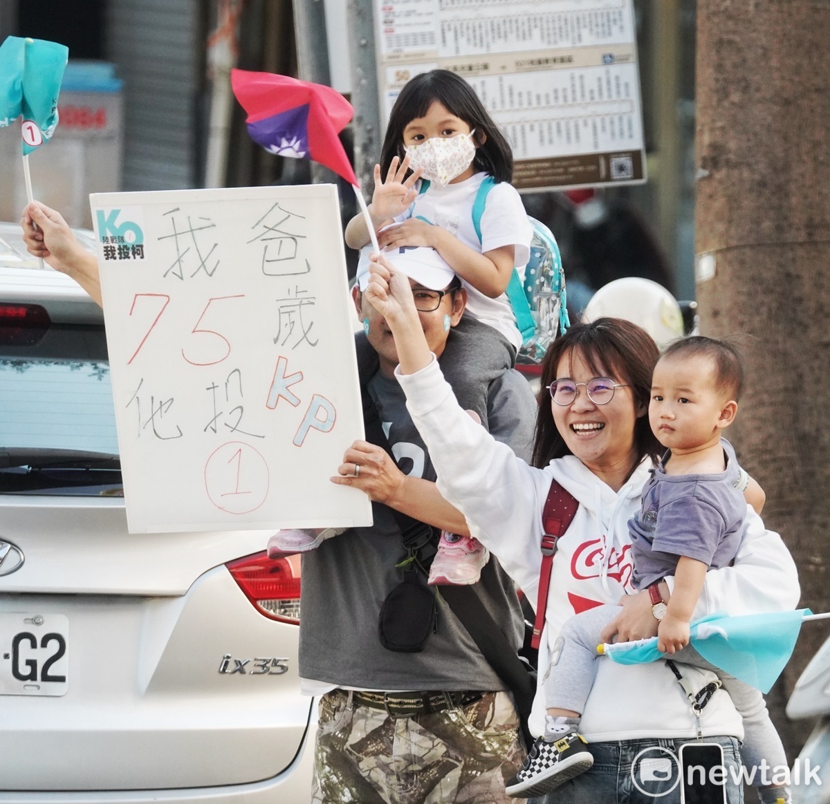 一對年輕夫婦抱著幼兒並高舉一張寫著：「我爸75歲他投KP」手舉牌，表達對柯的支持。 圖：張良一/攝
