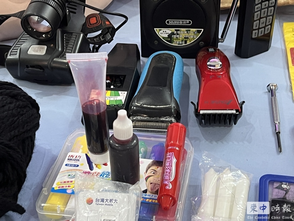 西哈努克省警察局於今日下午召開記者會，警方在現場展示了「晚安小雞」持有的鬼臉面具、衣服、軍裝、假槍、理髮器，以及用來冒充鮮血的紅色液體等工具。 圖：翻攝自柬中時報