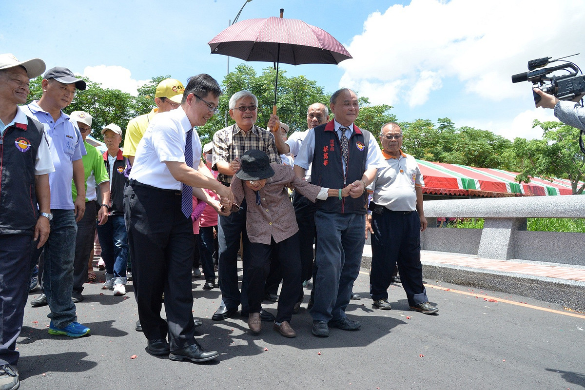 雲林縣長李進勇扶著造橋志工104歲盧林金阿嬤及所有志工共同試走虎尾科大興中分部新橋樑。 圖 : 雲林縣政府/提供