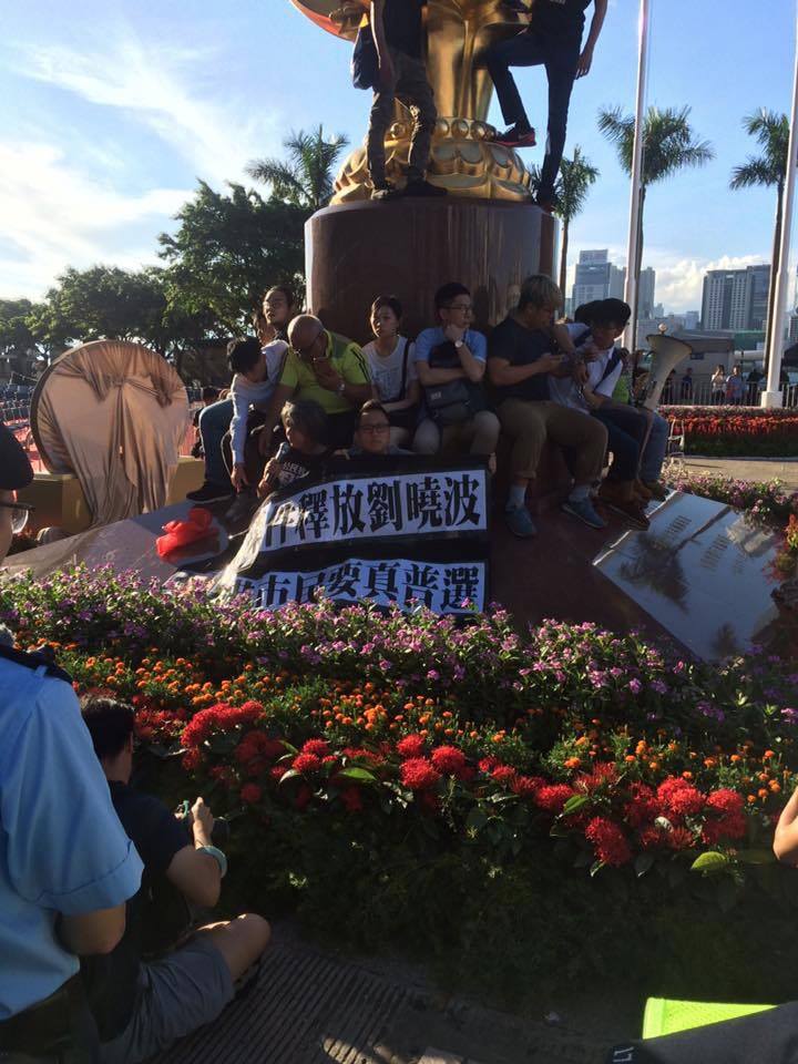 社會民主連線、香港眾志、人民力量和大專政關四個團體26人，今天(28日)下午圍繞金紫荊雕象進行靜坐請願行動，展示橫額提出 「無條件釋放劉曉波、香港人要真普選」。 圖:翻攝自香港眾志臉書