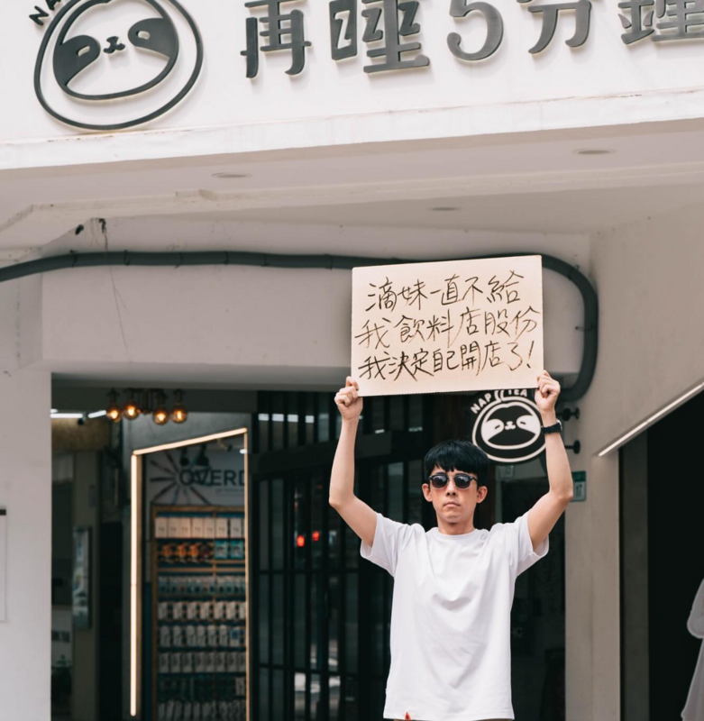 阿滴跑到滴妹的飲料店門口舉牌抗議「滴妹一直不給我飲料店股份」。 圖：翻攝自阿滴英文IG