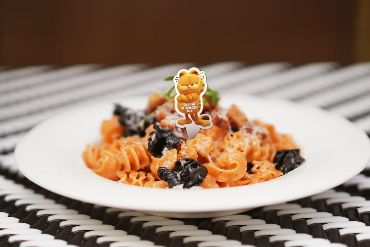 Pastaio推出「豬頰起司雙色麵」，麵體加入雞蛋、番茄糊、墨魚汁等原料，製成加菲貓橘黑配色。 圖：網銀國際影視／提供
