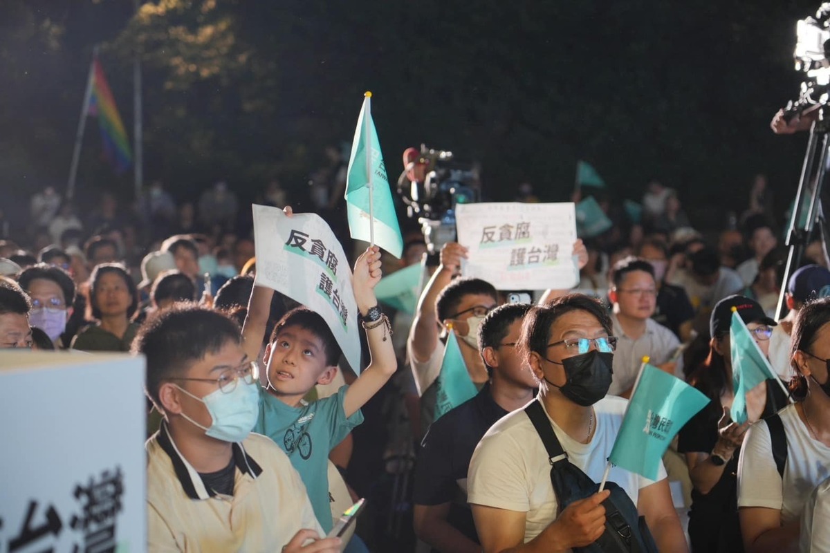 民眾黨今(22)天晚在榮星花園舉行「反貪腐、護台灣」宣講，儘管夏夜悶熱，但廣場仍聚集許多群眾，並高舉「反貪腐、護台灣」標語。 圖：擷取自台灣民眾黨臉書
