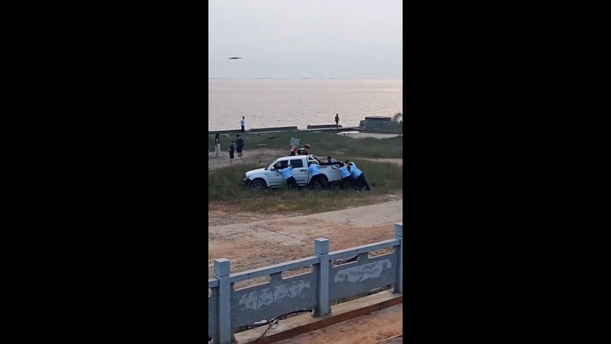 湖南省日前有一輛執法車陷入泥地中，執法人員只能想辦法把車推出來，民眾只願意圍觀，不願意提供幫助。 圖：擷取自 @fang_danie121 X 分享影片