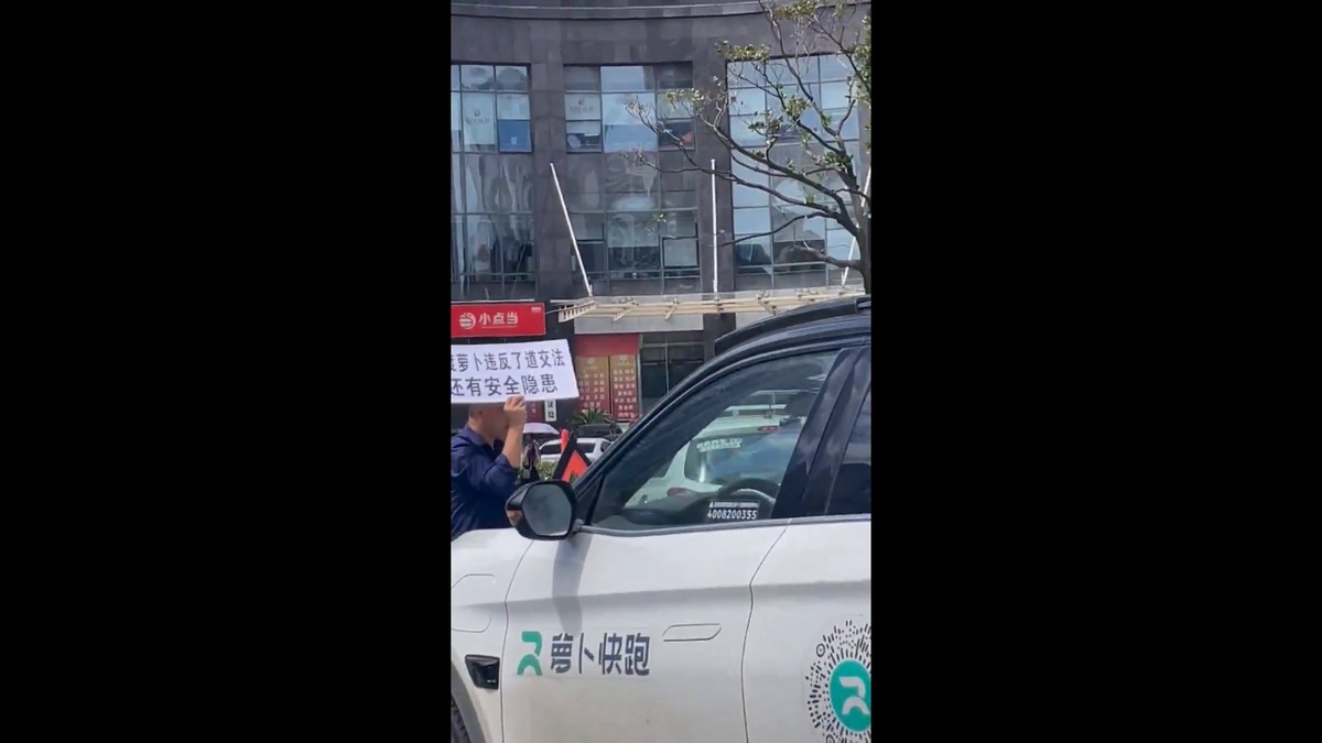 百度旗下的自動駕駛計程車品牌「蘿蔔快跑」自開始營運起便陷入許多爭議的漩渦之中。一名武漢男子手舉著蘿蔔快跑違法且存在安全隱患的牌子，在光天化日之下蘭亭蘿蔔快跑的車輛抗議。 圖：擷取自 @whyyoutouzhele X 帳號