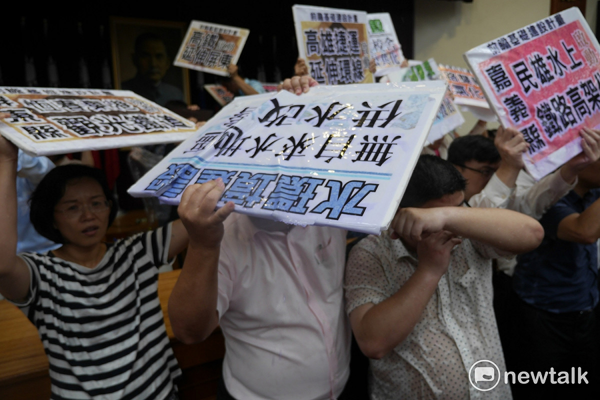 面對國民黨水球攻勢，綠委紛紛拿起看板或用手遮雨，但仍不敵雨勢，全身濕透。 圖：廖品瑄／攝