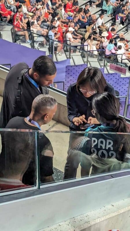 4日羽球男雙決賽時，不少人拍到這位中國女士拿著手機，在保全身邊指點沒收對象。中國異議人士表示，對台灣的比賽，中國一般都會派人到現場盯旗幟，再舉報給奧會。 圖：Sophia提供