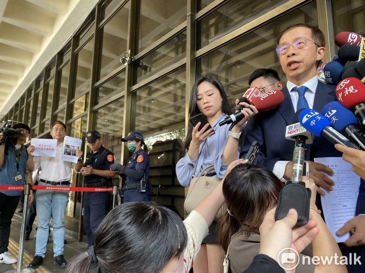 律師在受訪，民眾黨組織部主任林昭印在一旁舉牌抗議。 圖：周煊惠 / 攝