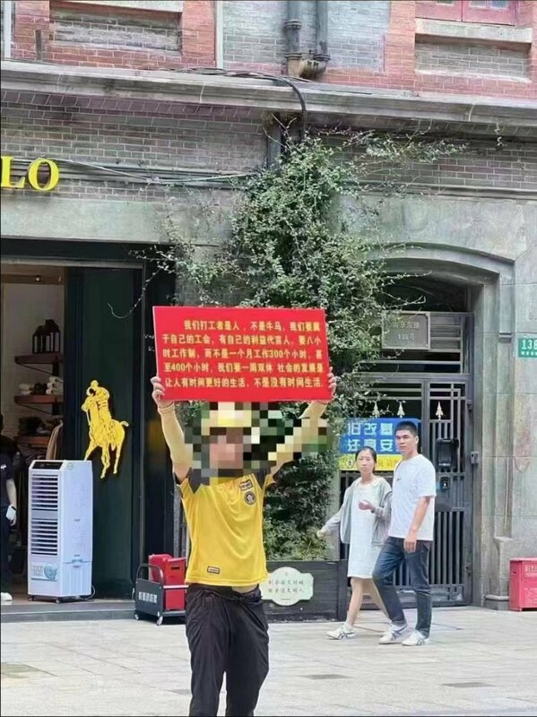 1 名美團外賣員在上海南京東路 138 號舉牌呼籲，中國社會需要做出改變。 圖：翻攝自李老師不是你老師 X 帳號