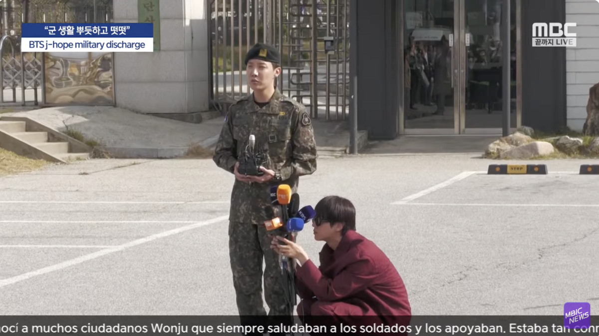 大哥JIN化身人體腳架，幫女記者拿近10支麥克風。 圖：攝自Youtube/엠빅뉴스