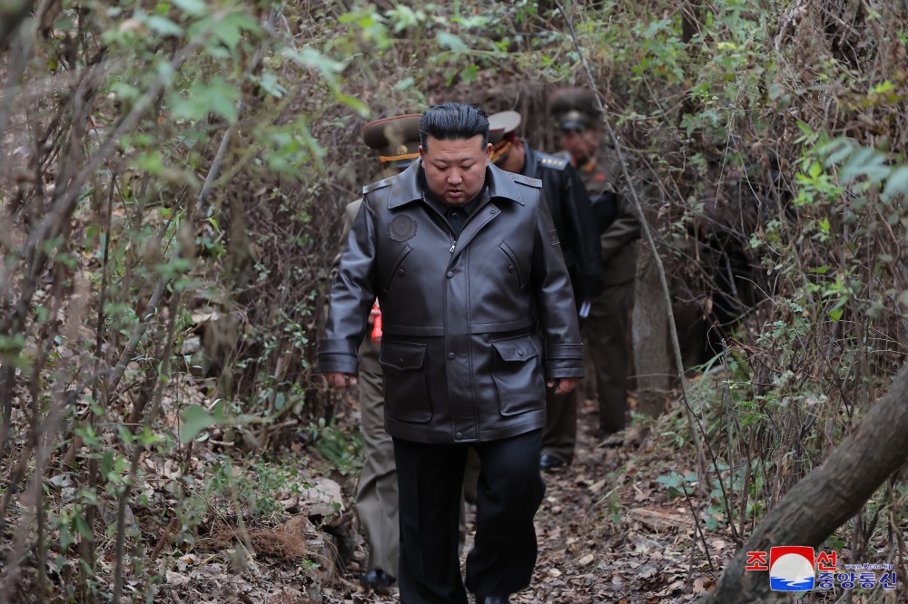 北韓領導人金正恩穿著帶有國務委員長標誌的黑色皮夾克率領視察高級幹部穿越林間小徑視察戰略導彈基地。 圖：翻攝朝中社