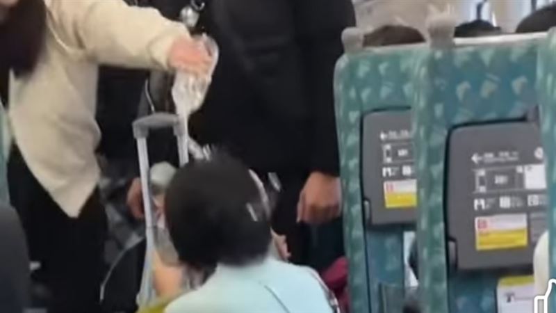 白衣女子站在高鐵走道間，將近半瓶礦泉水往蹲在地上的藍衣女子身上倒。 圖：翻攝自爆廢公社