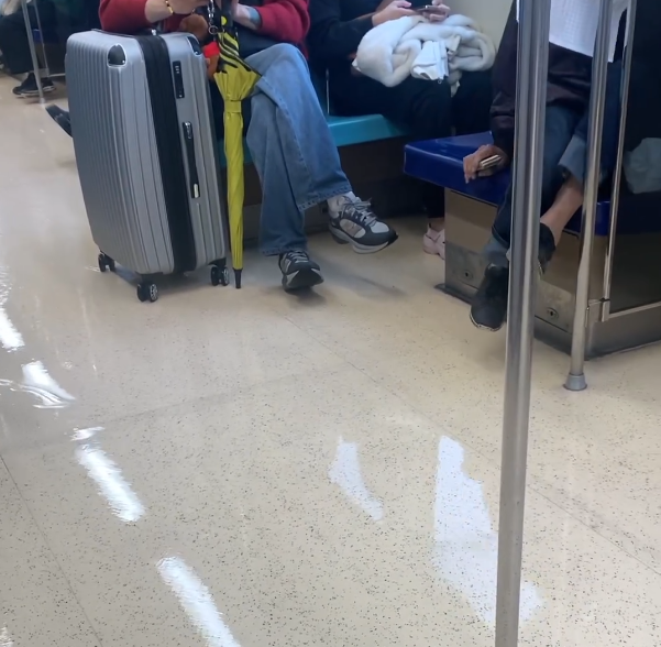 有網友搭乘捷運淡水線時，發現車廂地面「水淹成小溪」，抬頭一看卻發現所有乘客都舉起雙腿冷靜乘車。 圖：翻攝自threads影片