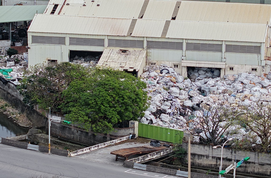 從遠處可看到大量廢塑料堆放滿到室外，堆放高度近一層樓。 圖：桃園市環保局/提供