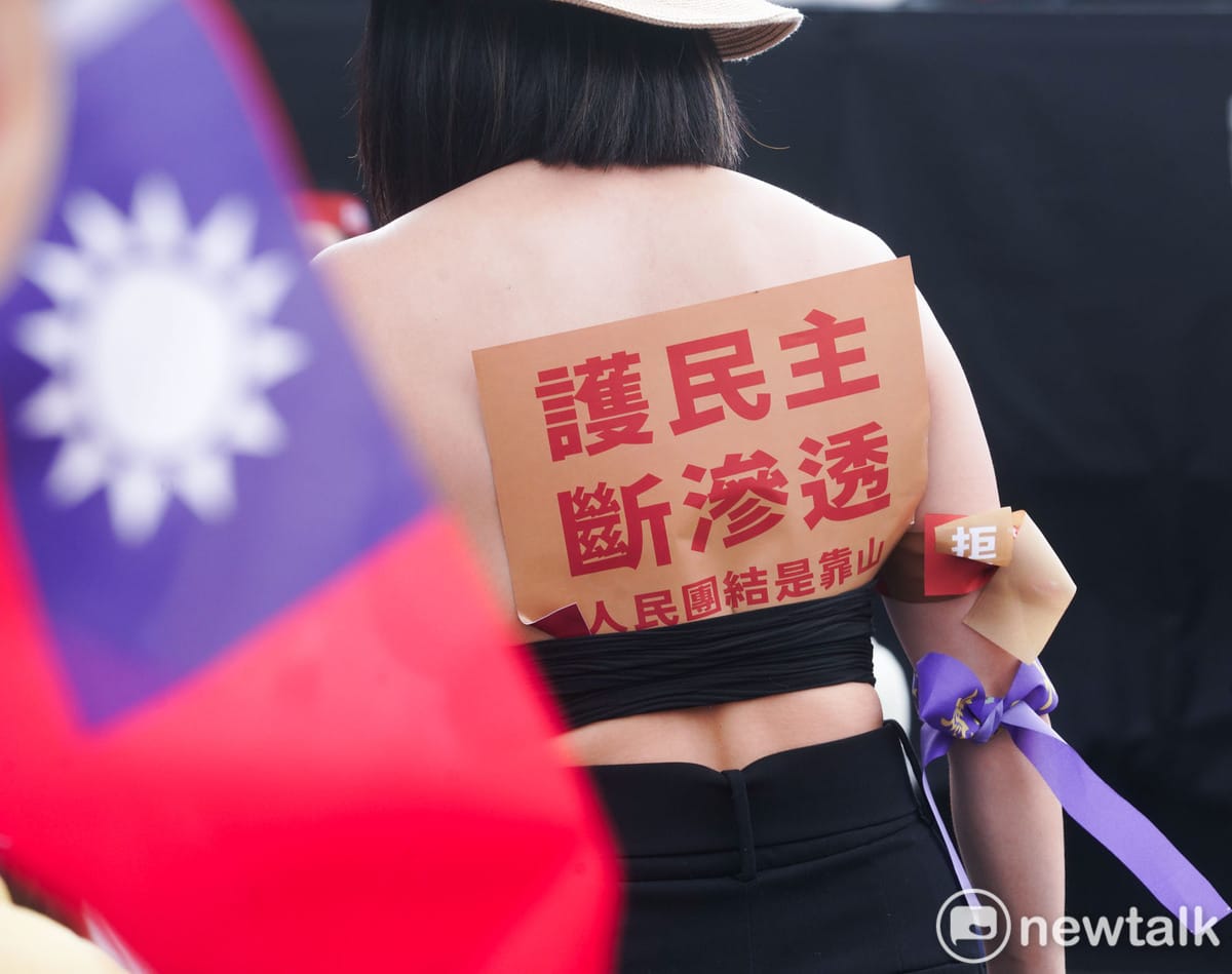 一位女性民眾將『護民主 斷滲透』的牌子在她的衣服背後。 圖：張良一 /攝