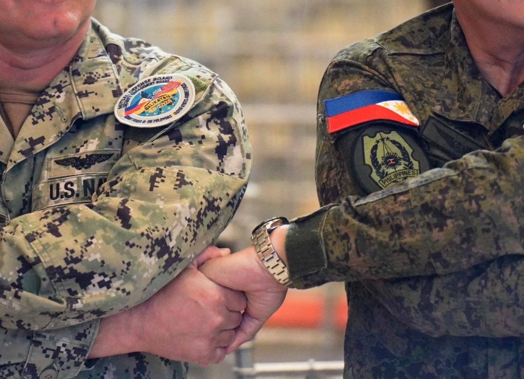 美國海軍與菲律賓武裝部隊軍官在第四十屆「肩並肩」開幕式上緊握手腕，展現堅定的聯盟精神與共同防衛承諾。雙方制服上的臂章與國旗清晰可見，象徵兩國肩並肩守護印太地區和平穩定。  圖／X@TeamAFP