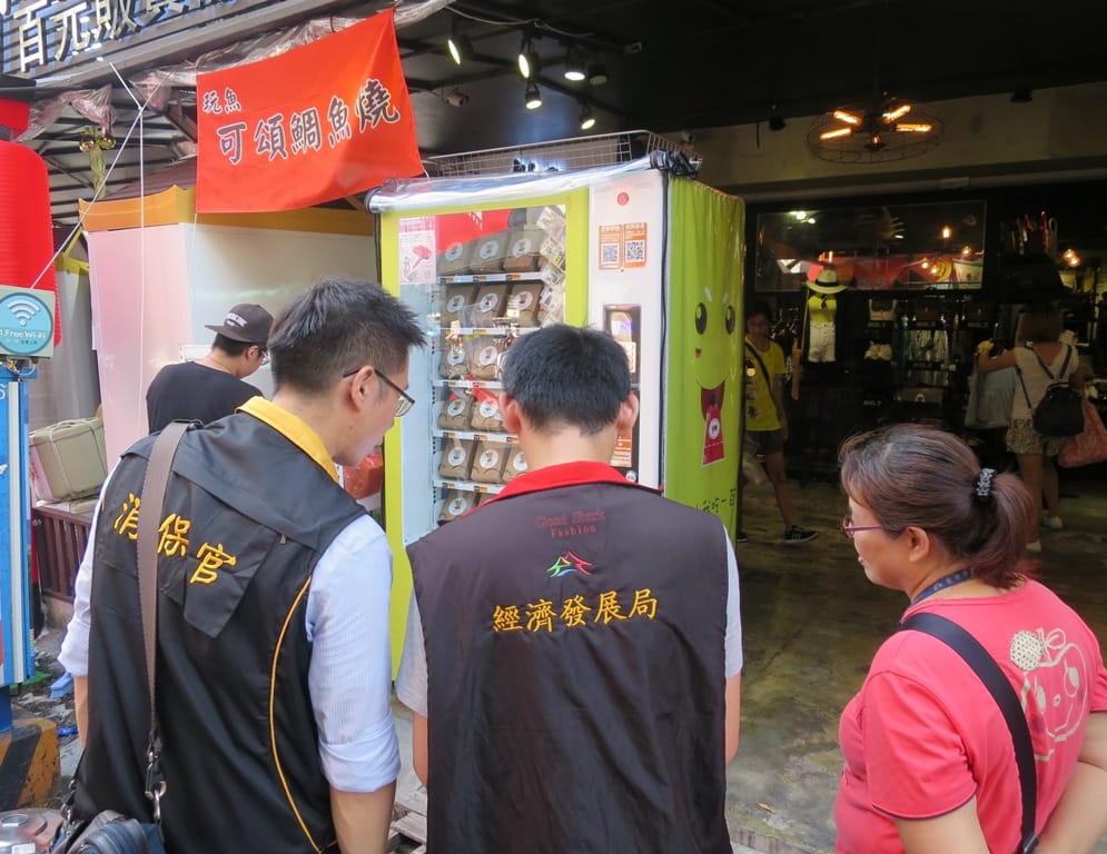 台中市政府消保官與經發局前往台中一中商圈進行稽查，發現市面上近三十台的百元販賣機皆未辦理營業登記，而且聯絡資訊僅有電話、臉書或是Line，沒有業者名稱或地址。 圖 : 台中市政府法制局 / 提供