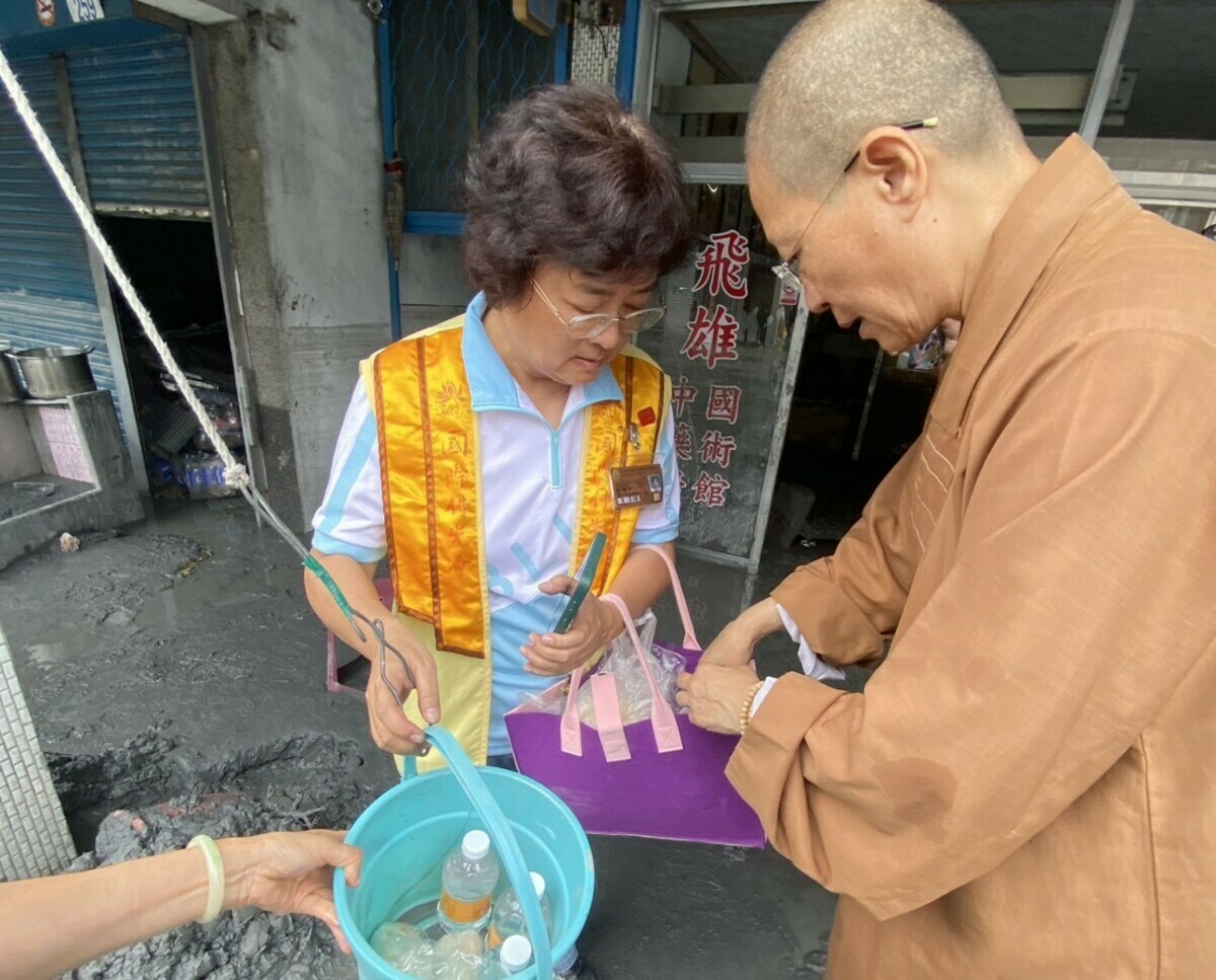 妙勳法師(右)和佛光人將帶去的飯糰、包子、燒餅、大悲咒水、觀世音菩薩聖像放進水桶，用拉繩方式交給災民。 圖：國際佛光會/提供