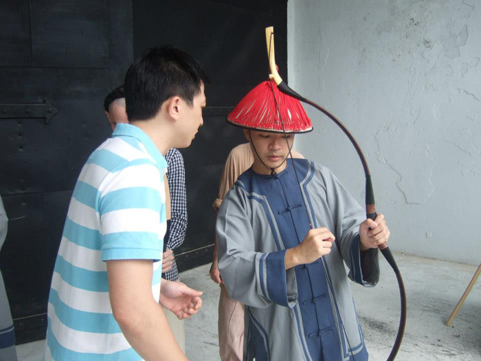 傳統弓愛好者組成的「飛雲射術俱樂部」教練，正在指導一名飾演清兵的演員如何用清代射法操作傳統弓。圖片來源：飛雲射術俱樂部提供