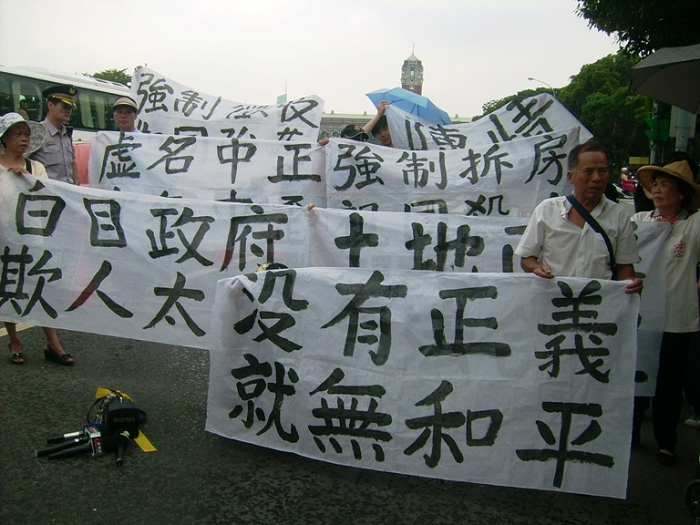 龍潭鄉中正路東側居民冒雨抗議政府姑息違建者，卻要來拆遷合法的私人土地，十分不合情理，也不合正義。圖片：符芳碩/攝