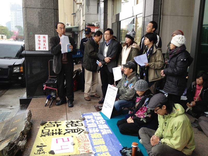 普安堂支持者今（19）日下午聚集在濕冷的文化部前，抗議文化部只會發公文的作法，對明早就要被強拆的普安堂來說緩不濟急。席地跪坐、戴灰色毛線帽者為普安堂發言人李榮台，從昨天下午2點開始絕食抗議，左一則為文化部文資局長施國隆。圖：王立柔/攝