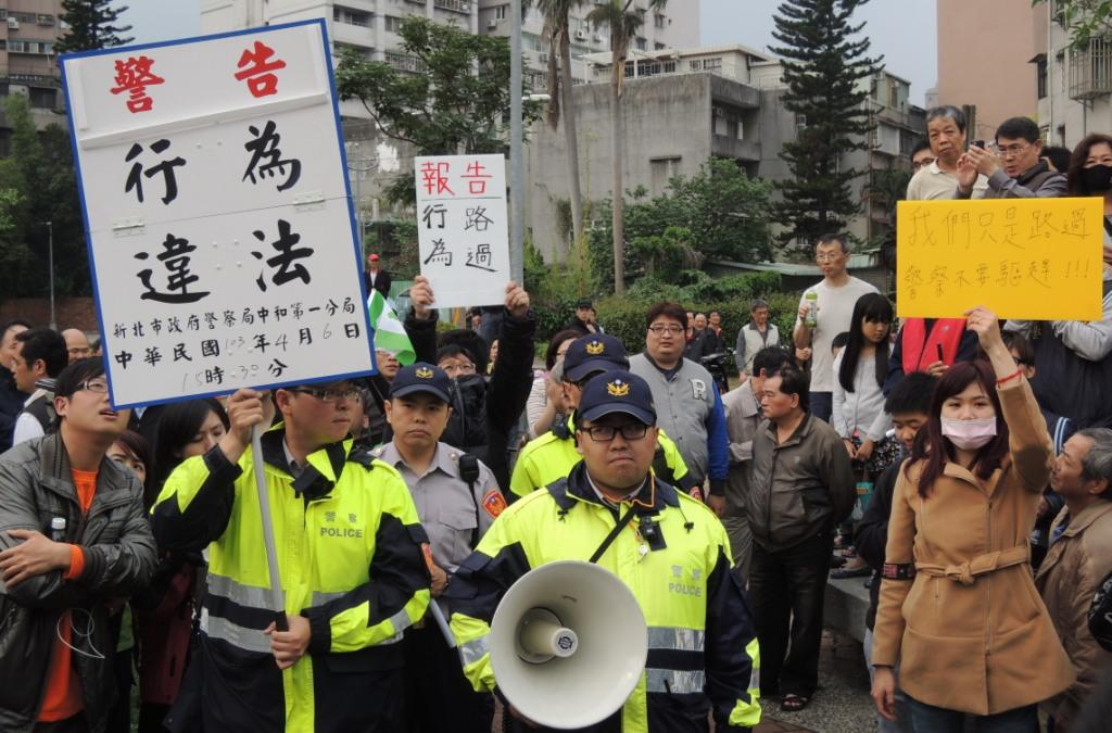 警方一度舉牌警告「行為違法」，卻遭民眾以高舉「我們只是路過，警察不要驅趕」、「報告，行為路過」的標語。圖：陳冠廷/攝