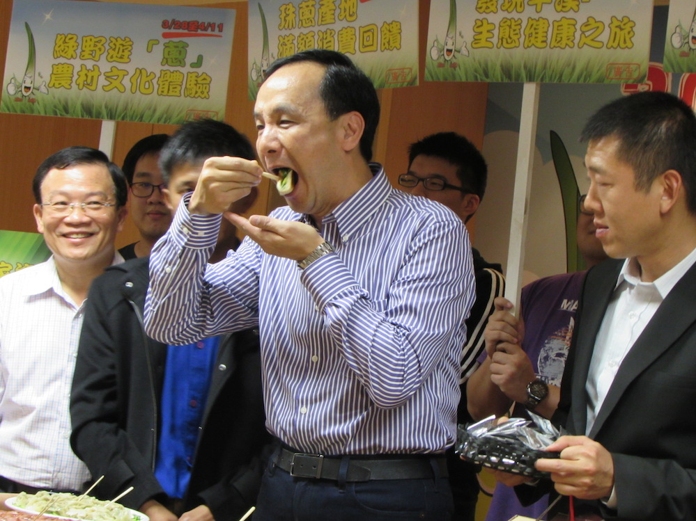 新北市長朱立倫16日下午參加新北市珠蔥上市記者會，大口品嘗特色伴手禮珠蔥餡餅。圖：邱珮文/攝