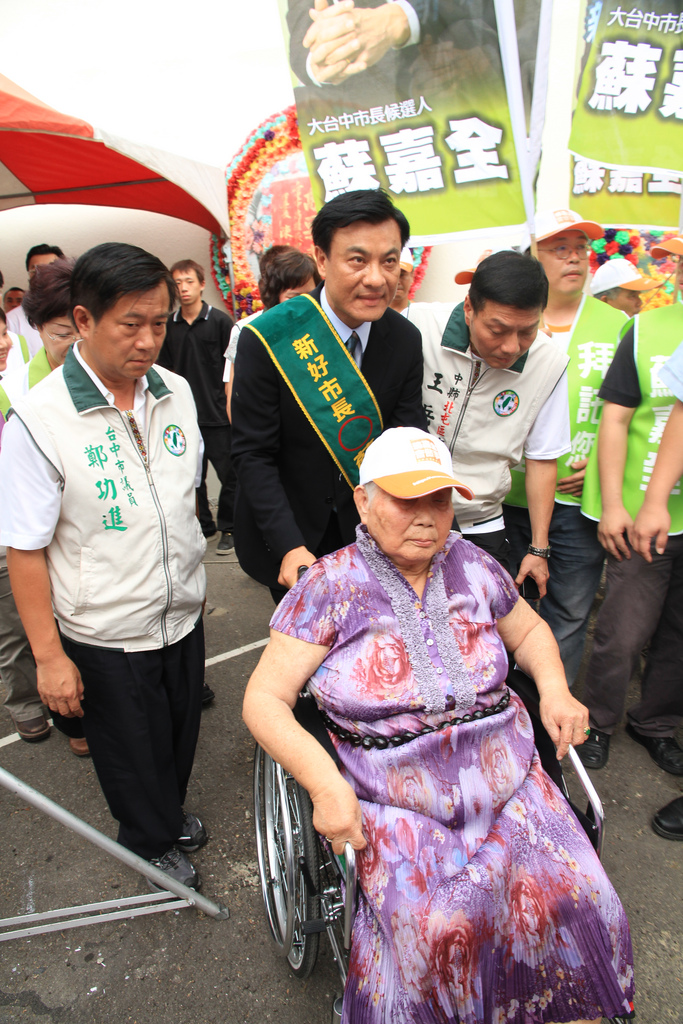 民進黨大台中市長候選人蘇嘉全推著兩眼雙盲、坐輪椅的岳母洪木蒞，進入競選總部會場。圖片來源：蘇嘉全競選總部