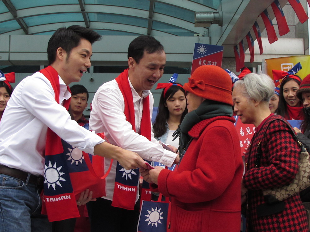 國民黨總統候選人朱立倫18日上午與立委候選人蔣萬安化身「暖男2人組」，披上國旗圍巾，在國民黨中央黨部前發送暖暖包、熱可可給民眾，圖：邱珮文/攝