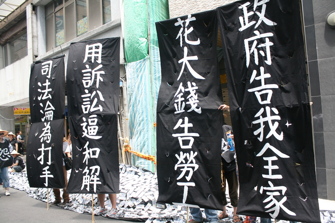 全國關廠工人連線的成員舉著「司法淪為打手」、「政府告我全家」、「用訴訟逼和解」及「花大錢告勞工」等4面大旗。圖：林良齊/攝