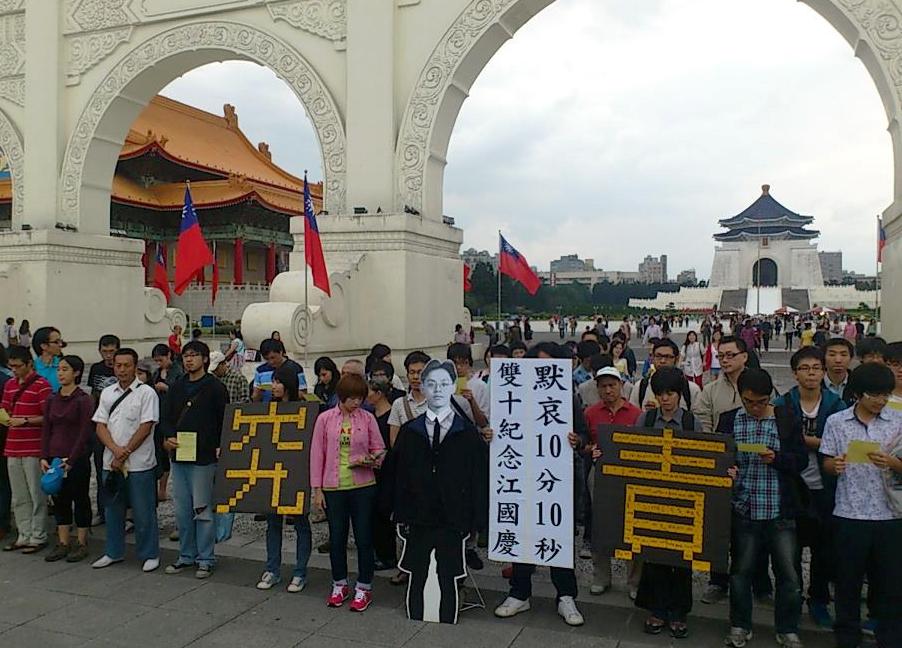 民間司法改革基金會志工及學生等數十人齊聚在自由廣場前，他們與江國慶的黑白人形立牌並肩而站，拿著「究責」標語，默哀10分10秒。他們也企盼早日起訴前空軍作戰司令陳肇敏，求償冤賠金。圖片來源：翻攝自許哲韡臉書