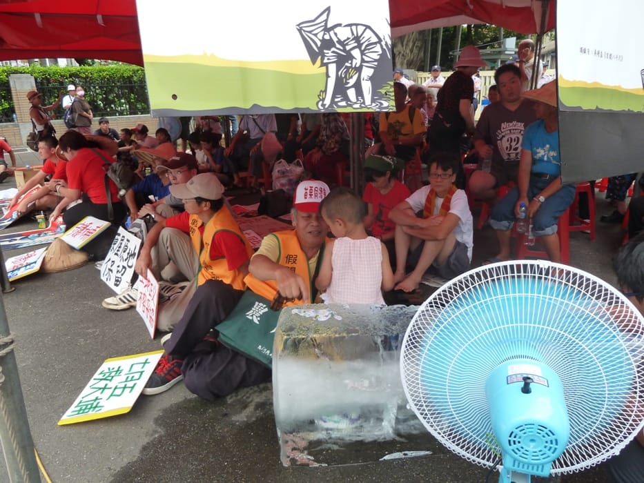 行政院門口聚集的大埔自救會等抗議群眾，在烈日下靠著冰塊和大風扇，從早上10點苦撐到下午5點多，仍未散去，現場警方已3度舉牌，隨時有可能驅離群眾。圖：謝莉慧/攝