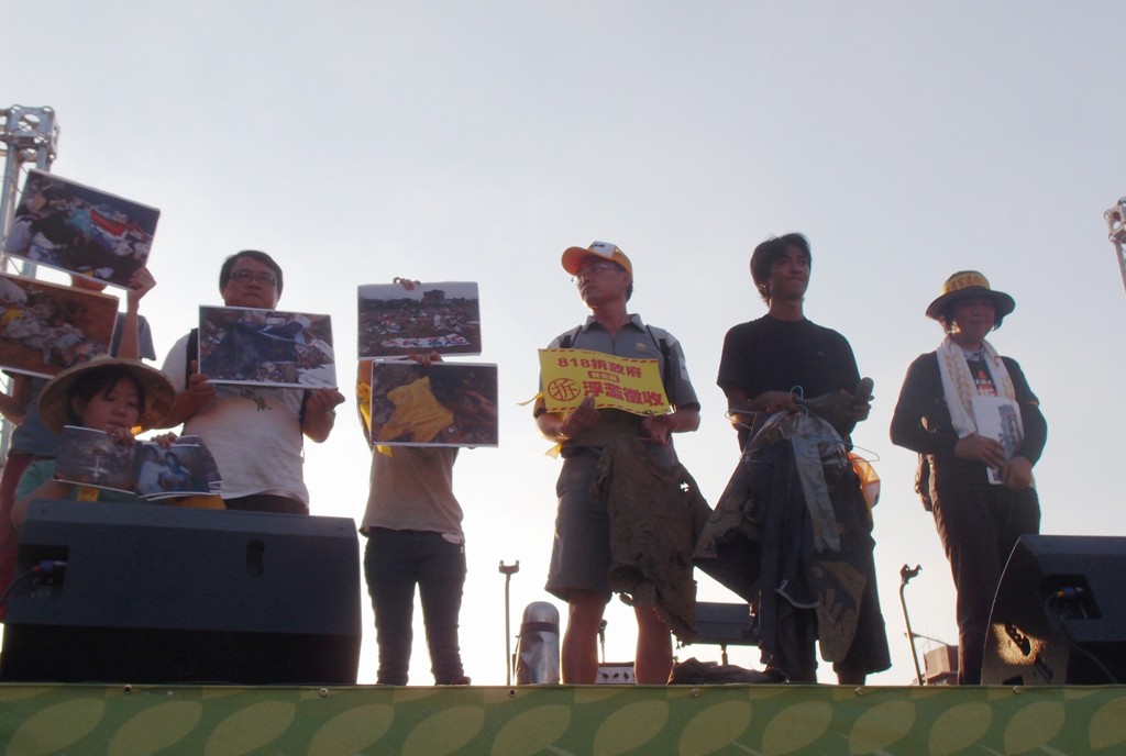 818拆政府晚會今（18）日登場，彭秀春(右)與兒子張元豪(右2)拿著瓦利堆中挖出的破爛衣物致詞。圖：陳柔伊/攝