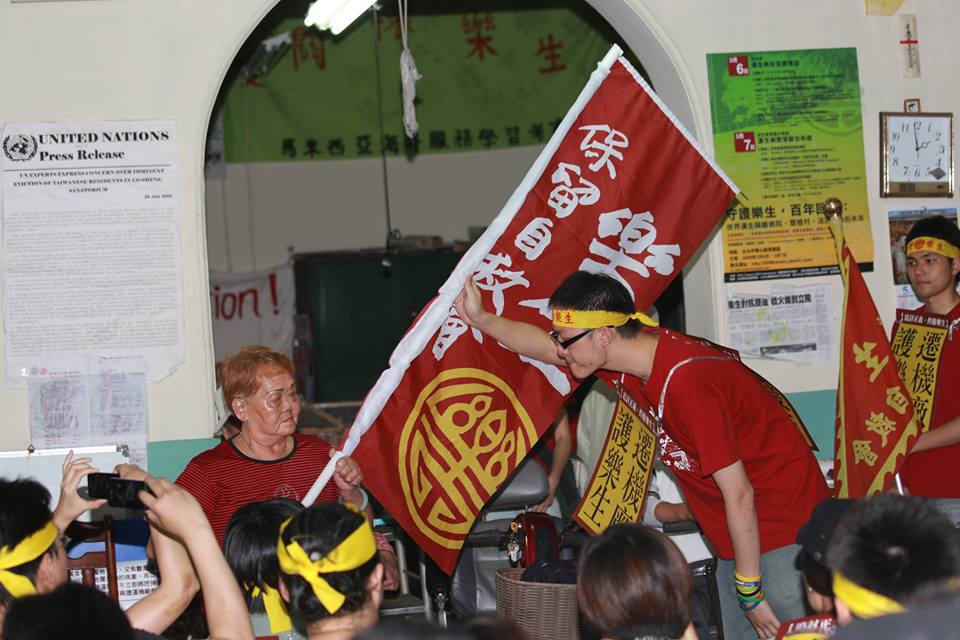 台大學生洪崇晏從樂生保留自救會的院民手上接過旗子。圖3之2：林雨佑/攝