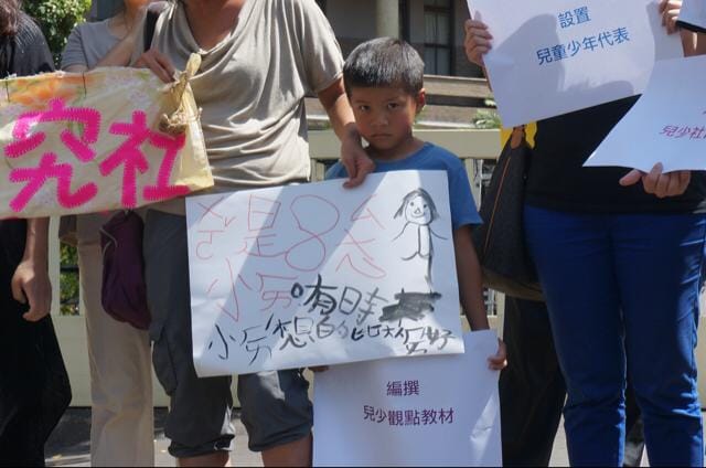 多個兒少團體今（5）日於行政院門口召開記者會陳情，多數團體也派出多位兒童及少年代表發言，現場有一位國小生特地請假來參加陳情，在他前面是他自己畫的畫，上面寫著「有時小孩想得比大人還好」。 圖：張容瑄/攝