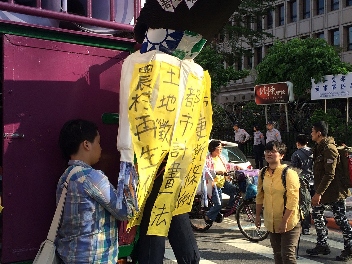 參與團體將掛滿圈地惡法布條的「惡人」玩偶，綁在遊行戰車後方，象徵藍綠兩黨的惡形惡狀。圖：楊淳卉/攝